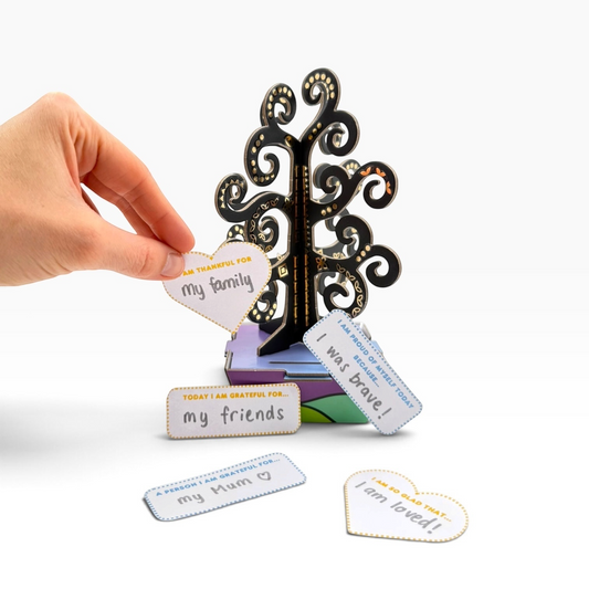 Eye Heart Golden Gratitude Tree sculpture kit with hand placing a heart-shaped note onto the black and gold tree